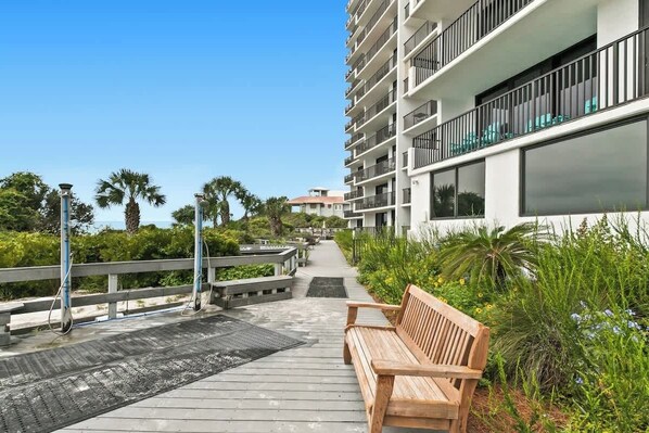 A wooden bench on a boardwalk with a view of a modern building with balconies and a clear sky.