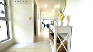 A hallway with a white console table, wicker baskets, and a large mirror. - Seabreeze on Dolphin (Agnes Water)