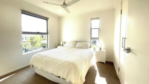 A bedroom with a bed, a ceiling fan, a window, and a door. - Seabreeze on Dolphin (Agnes Water)