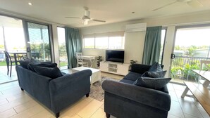 A modern living room with two sofas, a TV, and a balcony. - Seabreeze on Dolphin (Agnes Water)