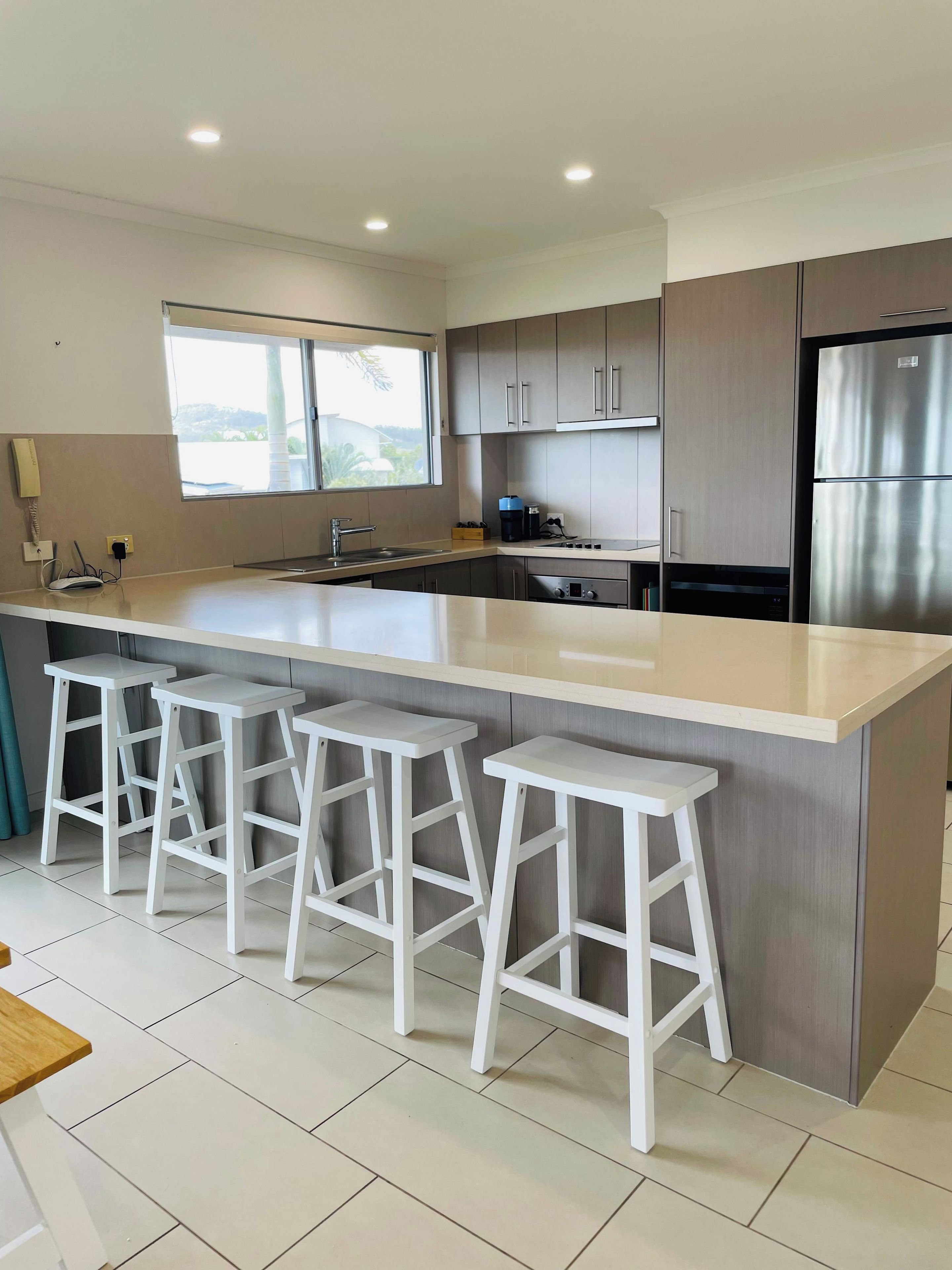 A modern kitchen with a large island, bar stools, stainless steel appliances, and a window providing natural light.