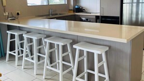 A modern kitchen with a large island, bar stools, stainless steel appliances, and a window providing natural light. - Seabreeze on Dolphin (Agnes Water)