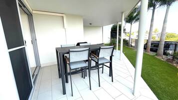 A covered patio area with a table and chairs, a sliding door, and a view of a well-maintained lawn and fence.