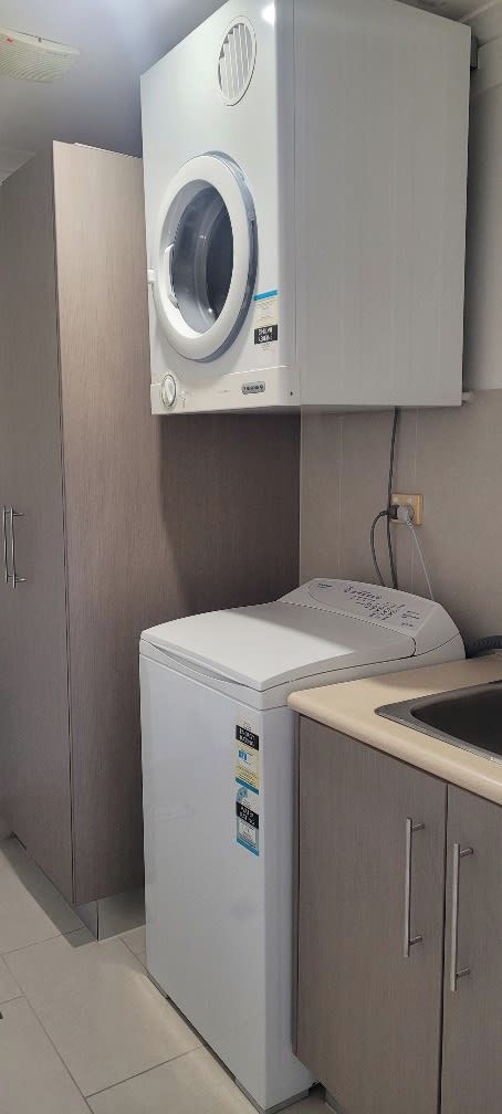 A compact laundry room with a front-loading washing machine and dryer, a sink, and wooden cabinets.