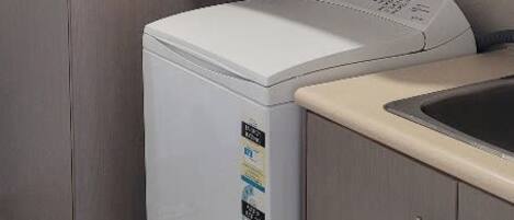 A compact laundry room with a front-loading washing machine and dryer, a sink, and wooden cabinets.