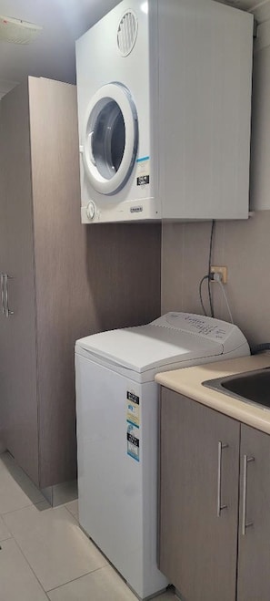 A compact laundry room with a front-loading washing machine and dryer, a sink, and wooden cabinets.