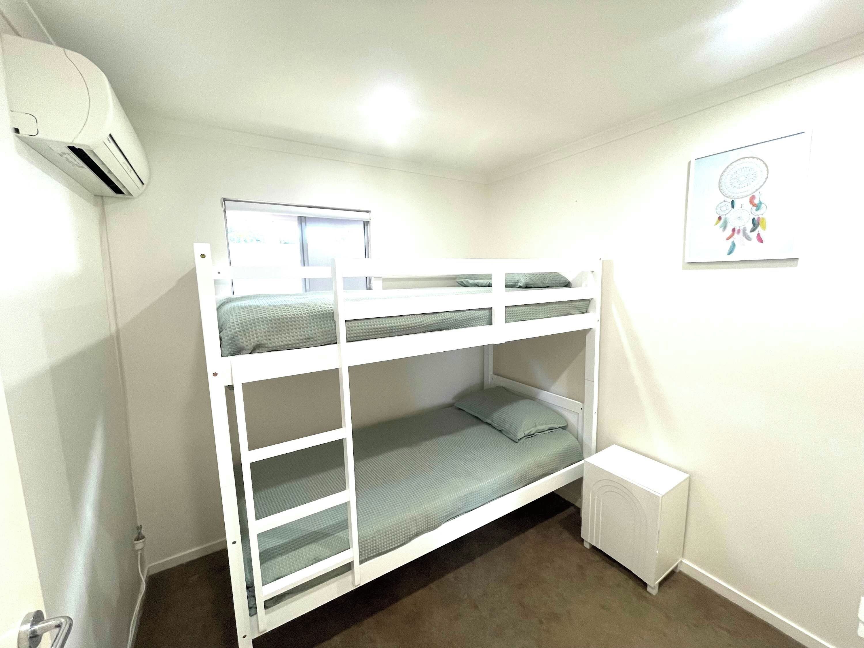 Une chambre avec un lit superposé, une fenêtre, un radiateur et un petit placard.