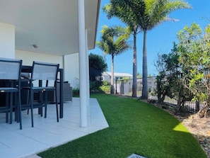 An outdoor patio area with a table and chairs, surrounded by a well-maintained lawn and tall palm trees.