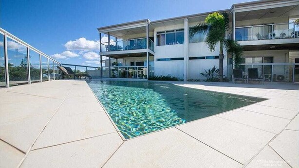 A modern building with a pool, glass railings, and outdoor seating. - Seabreeze on Dolphin (Agnes Water)