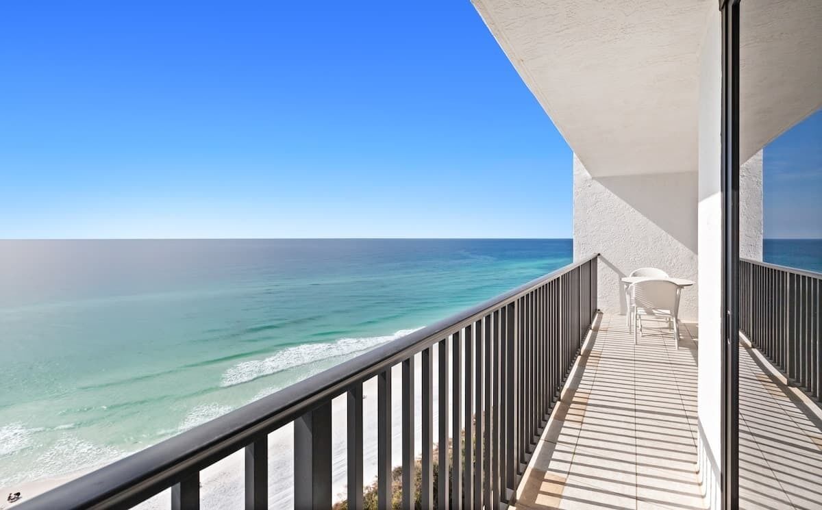 A balcony with a view of the ocean, a white chair, and a table.