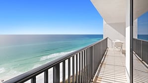 A balcony with a view of the ocean, a white chair, and a table.