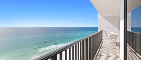 A balcony with a view of the ocean, a white chair, and a table.