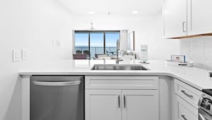 A modern kitchen with white cabinetry, a built-in dishwasher, and a large window offering a view of the sea.