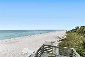A beach with a wooden walkway leading to the shore, a sign indicating beach rules, and a building on a hill in the background. - One Seagrove Place 1205 (Santa Rosa Beach)