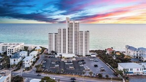 A high-rise hotel with multiple floors, a parking lot, and a view of the sea at sunset. - One Seagrove Place 1205 (Santa Rosa Beach)