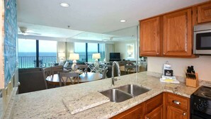 A kitchen with granite countertops, wooden cabinets, a stainless steel sink, and a stove. - One Seagrove Place 1205 (Santa Rosa Beach)