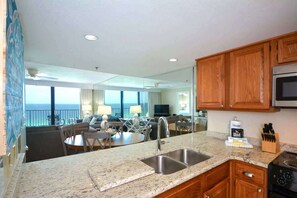 A kitchen with granite countertops, wooden cabinets, a stainless steel sink, and a stove. - One Seagrove Place 1205 (Santa Rosa Beach)