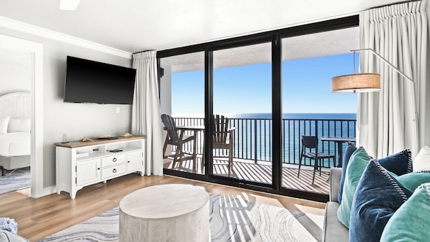 Een moderne hotelkamer met een balkon, een flatscreen televisie, een houten bureau en een bank met kussens.