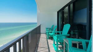 Un balcón con sillas Adirondack turquesa con vista a la playa.
