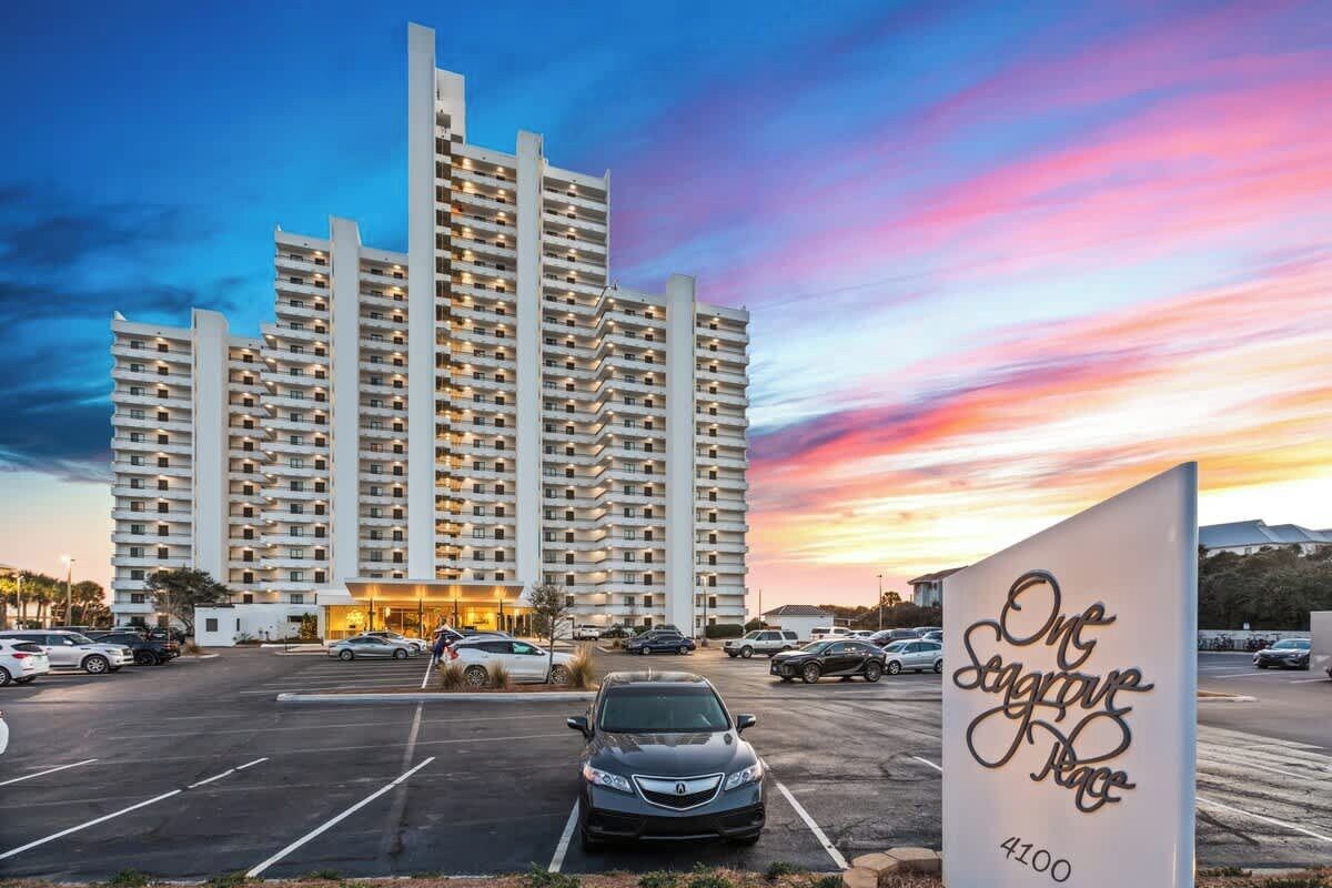 A high-rise hotel with multiple balconies, a parking lot, and a sign indicating 'One Seagrave Place 4100'.