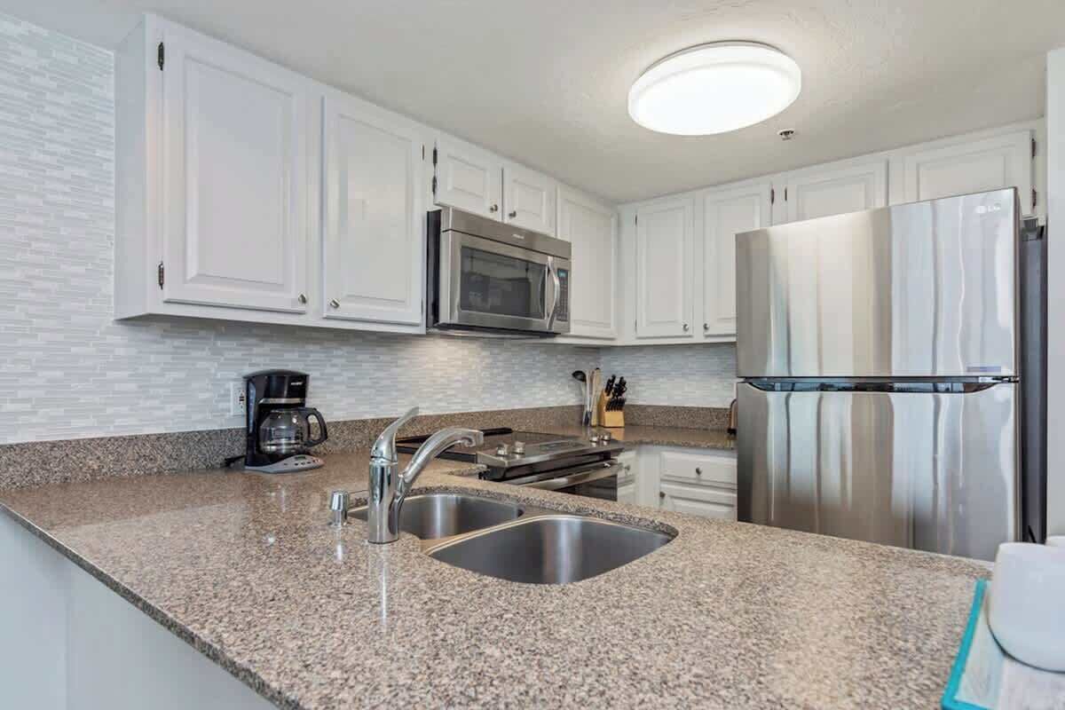 A kitchen with white cabinets, stainless steel appliances, granite countertops, and a coffee maker.