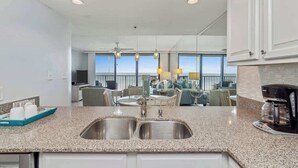 A modern kitchen with granite countertops, stainless steel sinks, and a coffee maker. - One Seagrove Place 0202 (Santa Rosa Beach)