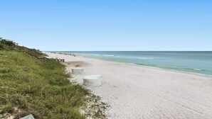 Une plage avec un ciel dégagé, un rivage sablonneux et quelques constructions blanches.