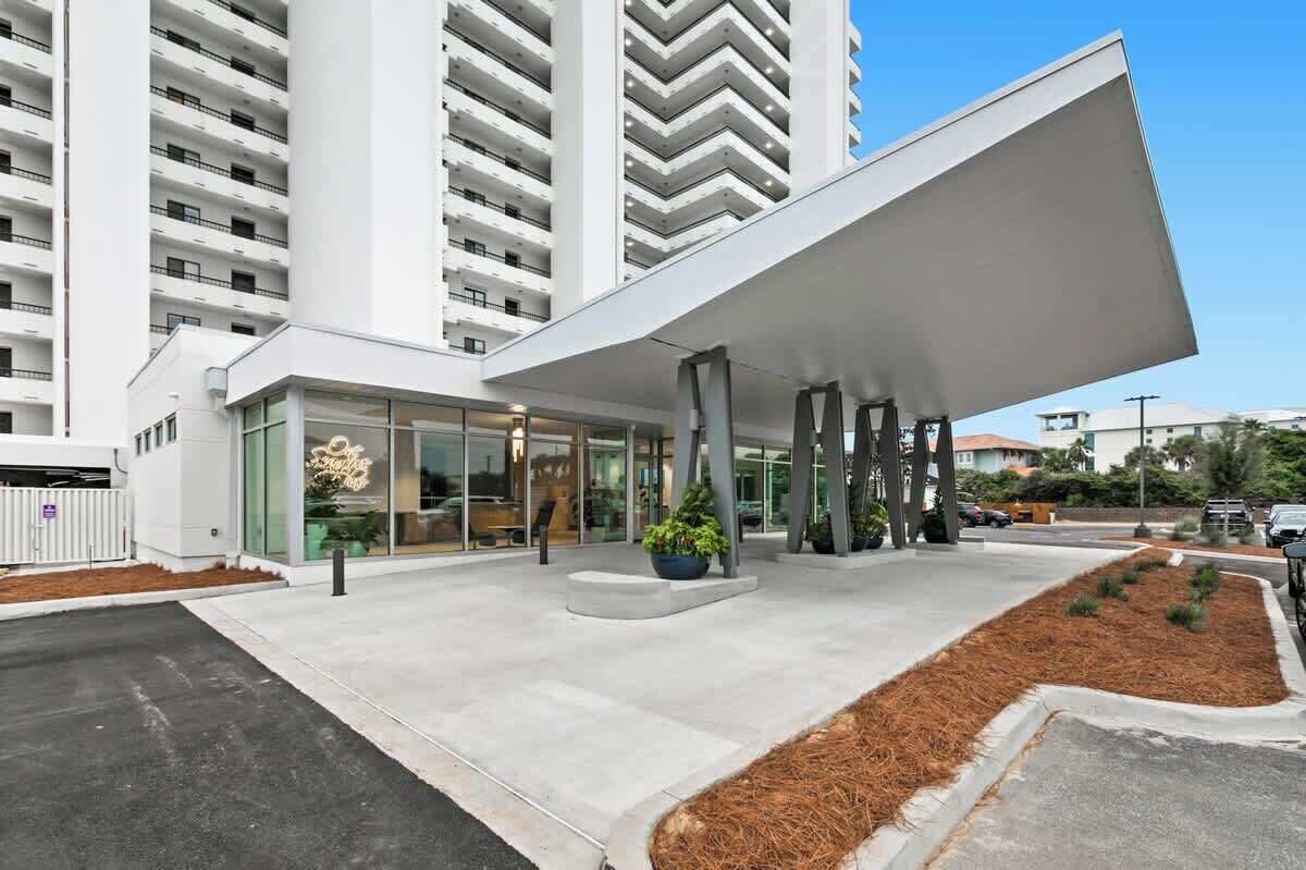 A modern hotel entrance with a glass facade, a covered outdoor area, and a parking lot.
