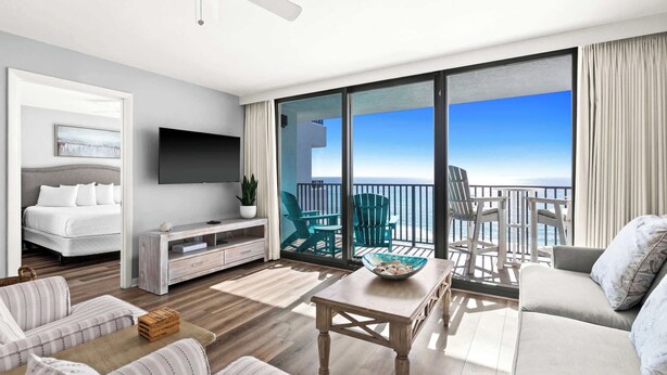 A modern hotel room with a balcony, a flat-screen TV, a bed, a seating area with a table, and a view of the ocean. - One Seagrove Place 0807 (Santa Rosa Beach)