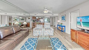 A spacious living room with a brown leather sofa, patterned armchairs, a coffee table, and a television.
