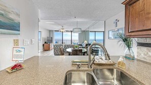 A modern kitchen with a large island, stainless steel sink, and a view of the ocean.