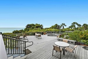 Eine Holzterrasse mit Außenmöbeln, mit Blick auf ein Gewässer und üppiges Grün.