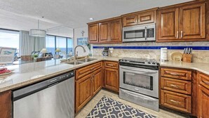 A modern kitchen with wooden cabinets, stainless steel appliances, and a large window offering a view.