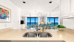 Une cuisine moderne dotée d’un évier à deux bacs, un coin repas offrant une vue sur l’océan et un salon avec une grande fenêtre donnant sur la mer.