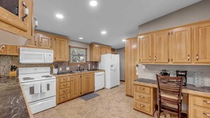 A kitchen with wooden cabinets, a white stove, a white refrigerator, and a wooden chair. - The Bird Nest- Bunkhouse, Sports Court, & Kayaks (Kingsland)