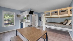 A compact room with a bunk bed, a small kitchenette, a dining table, and a window with a view of the outdoors. - The Bird Nest- Bunkhouse, Sports Court, & Kayaks (Kingsland)