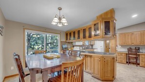 A spacious kitchen with wooden cabinets, a large island, and a dining area with chairs. - The Bird Nest- Bunkhouse, Sports Court, & Kayaks (Kingsland)
