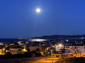 A coastal town at night with a bright moon in the sky, streetlights, and buildings along the waterfront. - Holiday flat with balcony and sea view (La Caletta)