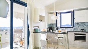 A modern kitchen with a large window, a dining area with two chairs, and a balcony with a chair and a table. - Holiday flat with balcony and sea view (La Caletta)