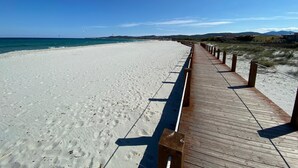 A wooden boardwalk leading to a sandy beach with clear blue water and distant hills. - Holiday flat with balcony and sea view (La Caletta)
