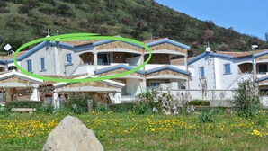 A residential building with multiple balconies, a stone facade, and a hillside backdrop. - Holiday flat with balcony and sea view (La Caletta)
