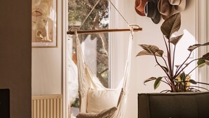 Een kamer met een hangstoel van macramé, een kamerplant en een verzameling hoeden aan een muur.