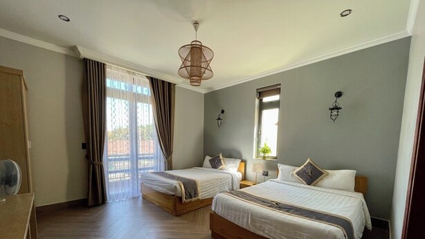 A hotel room with two beds, a wooden floor, a ceiling fan, a window with curtains, and a hanging light fixture. - Hai An villa Hotel (Lam Vien - Da Lat)