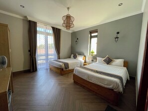 Habitació d'hotel amb dos llits, un sòl de fusta, un ventilador de sostre, una finestra amb cortines i una làmpada penjant.