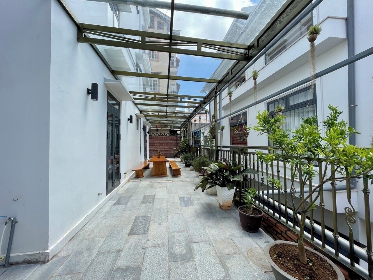 A covered corridor with a bench, potted plants, and a railing.
