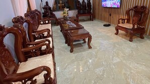 A spacious living room with a long wooden coffee table, ornate wooden chairs, a television, and a decorative statue. - Hai An villa Hotel (Lam Vien - Da Lat)