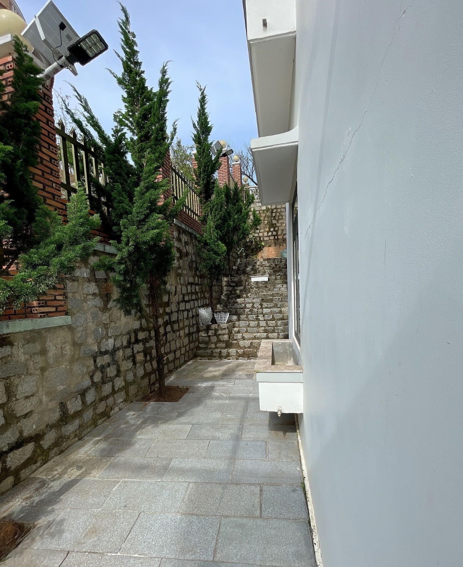 Un étroit sentier de pierres mène à un bâtiment blanc doté d’un panneau solaire et surmonté d’un petit arbre.