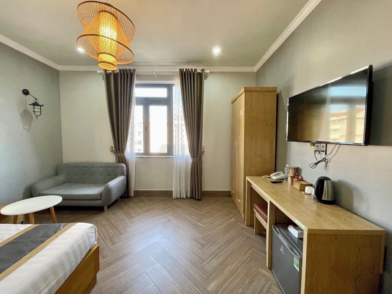 Ein Hotelzimmer mit einer Sitzecke, einem kleinen Tisch, einem Schreibtisch mit Fernseher, einem Kleiderschrank und einem Fenster mit Vorhängen.