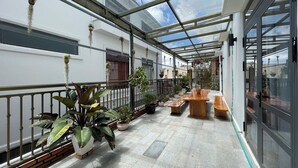A covered outdoor patio with potted plants, wooden benches, and a glass door leading to a building. - Hai An villa Hotel (Lam Vien - Da Lat)