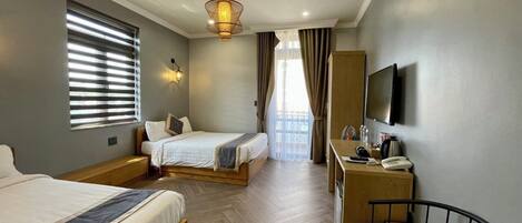 A hotel room with two beds, a desk, a chair, a TV, and a balcony with curtains.